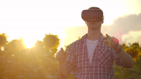 A-young-scientist-in-plaid-shirt-and-jeans-uses-VR-glasses-on-the-field-with-sunflowers-for-scientific-article.-These-are-modern-technologies-in-summer-evening.